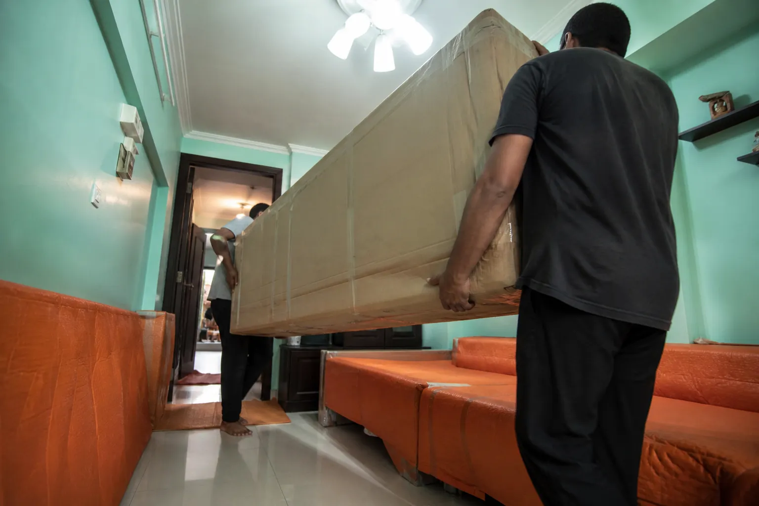 Installers moving a sofa bed component through a Mumbai corridor