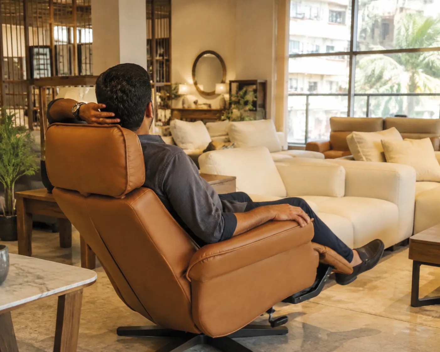 Client testing a tan recliner in a warm Mumbai showroom