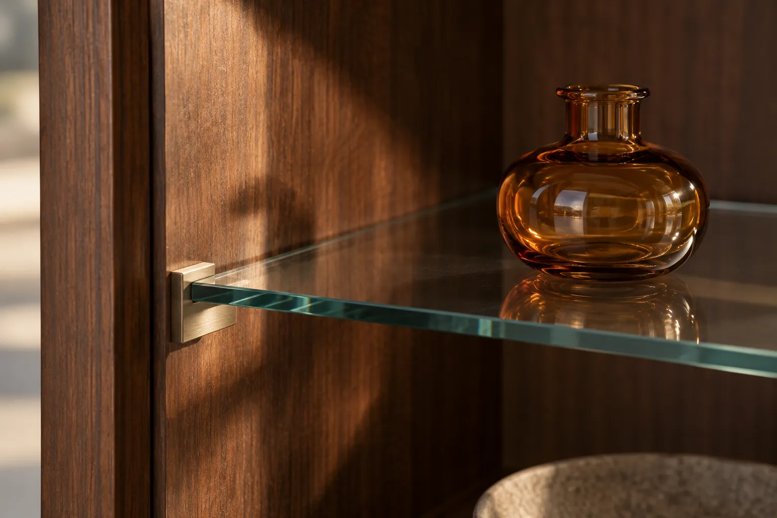 Close-up of a glass shelf support and amber vase inside a walnut cabinet
