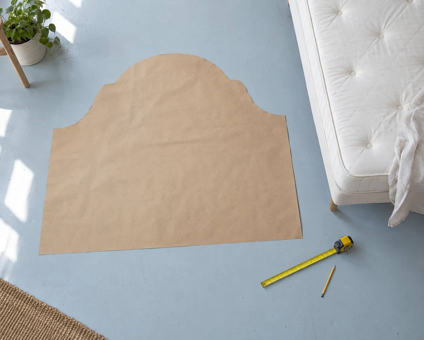 Headboard-shaped kraft paper template with tape measure on a pale blue floor.